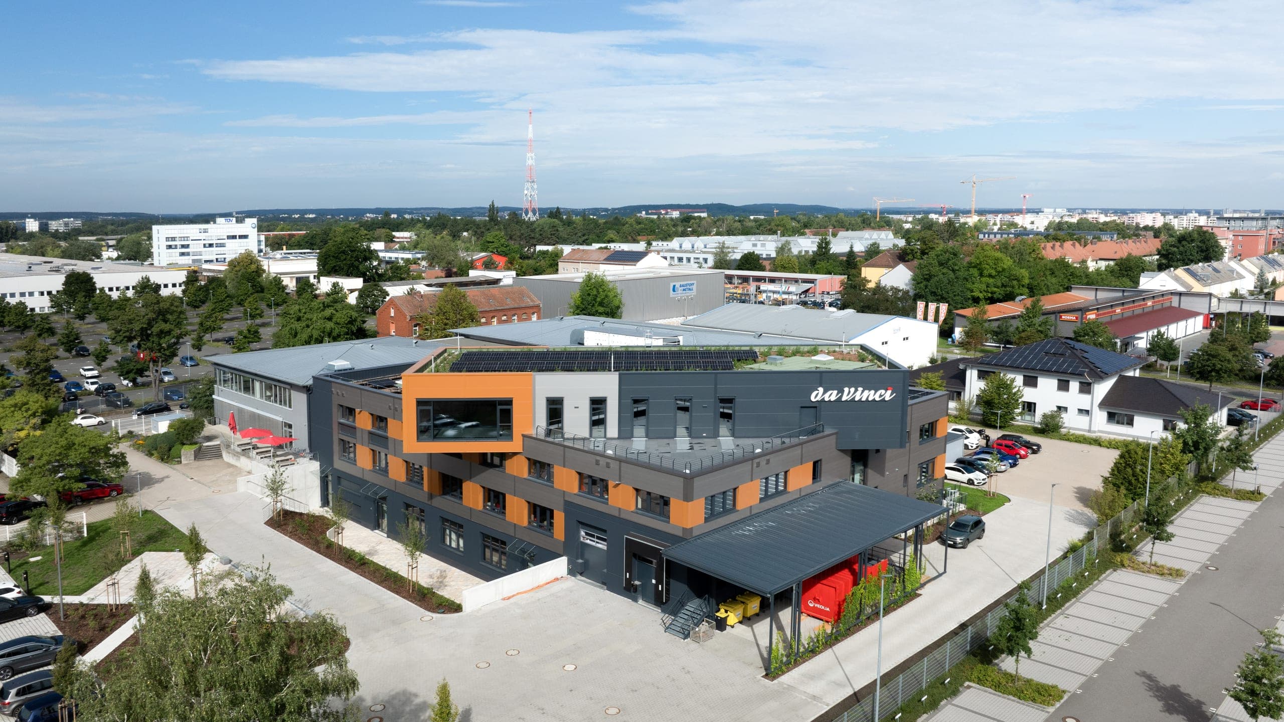 Fertigungshalle daVinci in Nürnberg, Luftbild mit orangefarbenem Kragbaukörper und Photovoltaik auf dem Gründach