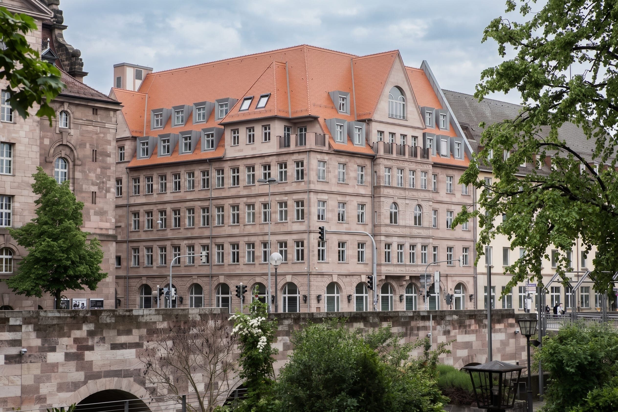 Büro- und Wohngebäude Deutscher Hof in Nürnberg, Blick über eine Sandsteinmauer mit Bäumen im Vordergrund