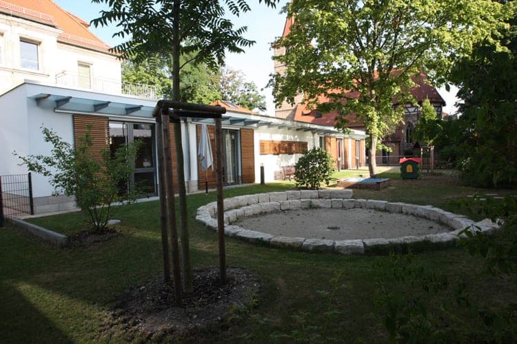 Gemeindezentrum der Johanneskirche in Nürnberg, Blick aus dem Garten mit Sandspielfläche und Baumbestand